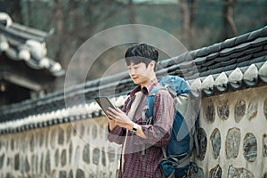 young man backpacking in Korea. Using a tablet computer leaning against a wall