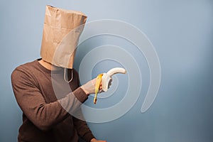 Young man with bag over his head using banana as gun