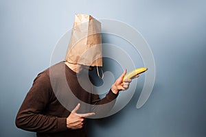 Young man with bag over his head using banana as gun