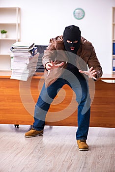 Young man in balaclava stealing information from the office