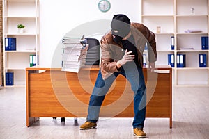 Young man in balaclava stealing information from the office