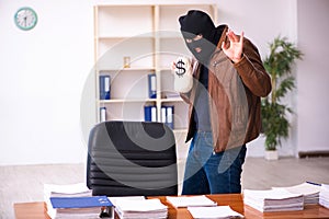 Young man in balaclava stealing information from the office