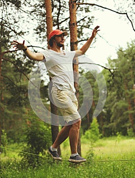 Young man balancing his arms walk on a loose rope tied between two trees, male training slack rope walking, slacklining in summer