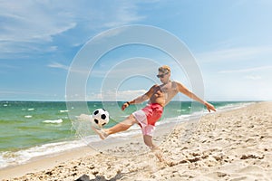 Young man with ball playing soccer on beach