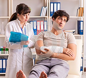 Young man with bandaged arm visiting female doctor traumatologis