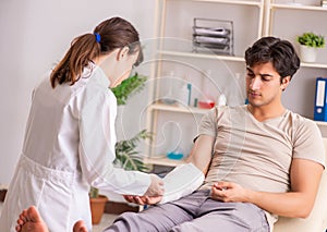 Young man with bandaged arm visiting female doctor traumatologis