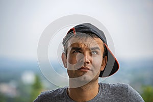 Young man in a baseball cap ponders some idea by lifting up his