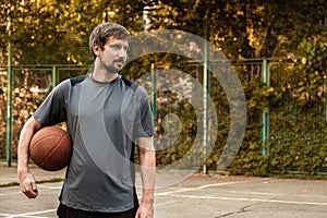 A young man with a basketball ball in his hand on an open sports court. Sports concept