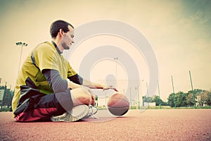 Young man on basketball court. Sitting and dribbling