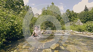 Young man bathing in river water and shaking wet hair slow motion