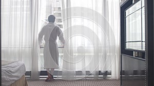 Young man in bathrobe admire view form the window in the morning. 4k