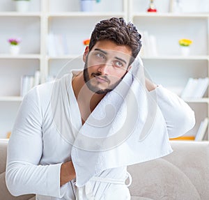 Young man in a bathrobe after shower drying hair with a towel