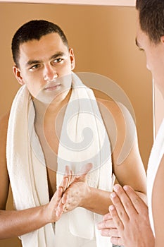 Young man in the bathroom's mirror using cream