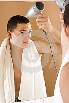 Young man in the bathroom's mirror using hair drier