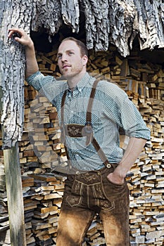 Young man in bavarian lederhosen in front of firewood photo