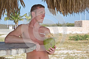 Young man on the beach drinking from coconut