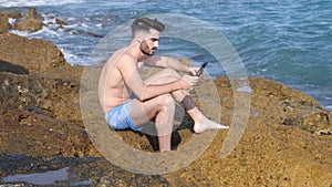 Young man on beach reading with ebook reader