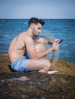 Young man on beach reading with ebook reader