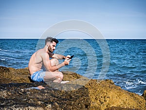 Young man on beach reading with ebook reader