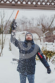 A young man with a beard in a blue jacket cleans snow with a shovel in his area 1