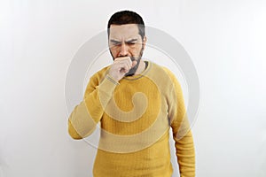 Young man with beard coughs while covering his mouth with his closed fist