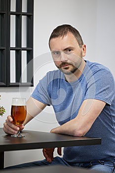 A young man with a beard drinks beer from a glass in a cafe