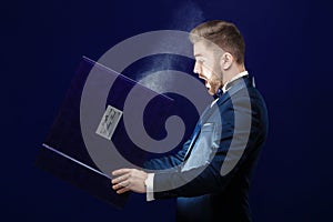 Young man with beard holding book and magic light on dark background