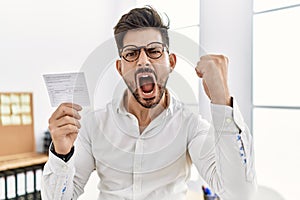 Young man with beard holding covid record card annoyed and frustrated shouting with anger, yelling crazy with anger and hand