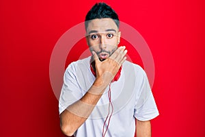 Young man with beard listening to music using headphones looking fascinated with disbelief, surprise and amazed expression with