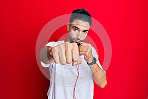 Young man with beard listening to music using headphones punching fist to fight, aggressive and angry attack, threat and violence