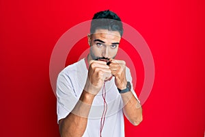 Young man with beard listening to music using headphones ready to fight with fist defense gesture, angry and upset face, afraid of