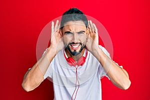 Young man with beard listening to music using headphones trying to hear both hands on ear gesture, curious for gossip