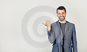 The young man with a beard, looking and pointing to the side with a thumb at a place for advertising, look here