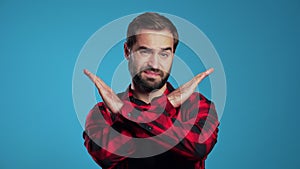 Young man with beard making no crossing hands sign, negation gesture over blue studio background