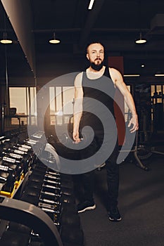 A young man with a beard is posing in the gym with dumbbells