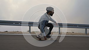 Young man with a beard riding skateboard cruising downhill on countryside road