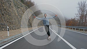 Young man with a beard riding skateboard cruising downhill on countryside road