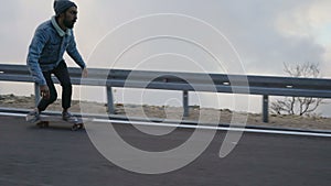 Young man with a beard riding skateboard cruising downhill on countryside road