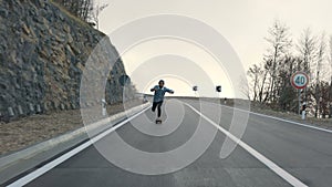 Young man with a beard riding skateboard cruising downhill on countryside road