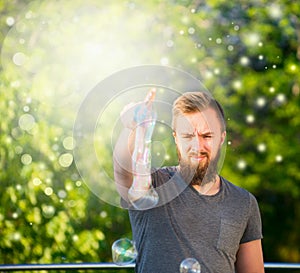 Young man with a beard spending time in nature, making soap bubbles nature background with bokeh