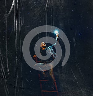 A young man with a beard on the stairs holds a star against the background of the night sky with scratches. creative concept