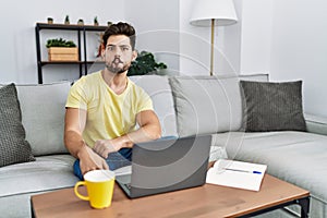 Young man with beard using laptop at home making fish face with lips, crazy and comical gesture