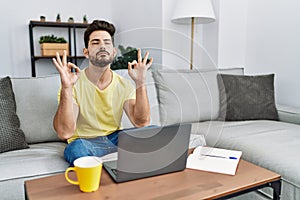 Young man with beard using laptop at home relax and smiling with eyes closed doing meditation gesture with fingers