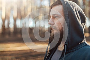 A young man with a beard walks in a pine forest. Portrait of a brutal bearded man in a hood