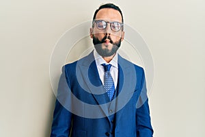 Young man with beard wearing business suit and tie making fish face with lips, crazy and comical gesture