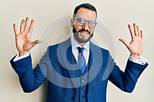 Young man with beard wearing business suit and tie showing and pointing up with fingers number ten while smiling confident and