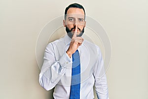 Young man with beard wearing business tie asking to be quiet with finger on lips
