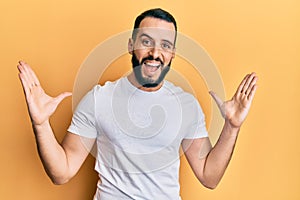 Young man with beard wearing casual white t shirt celebrating victory with happy smile and winner expression with raised hands