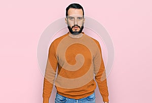 Young man with beard wearing casual winter sweater with serious expression on face