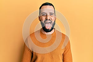 Young man with beard wearing casual winter sweater sticking tongue out happy with funny expression